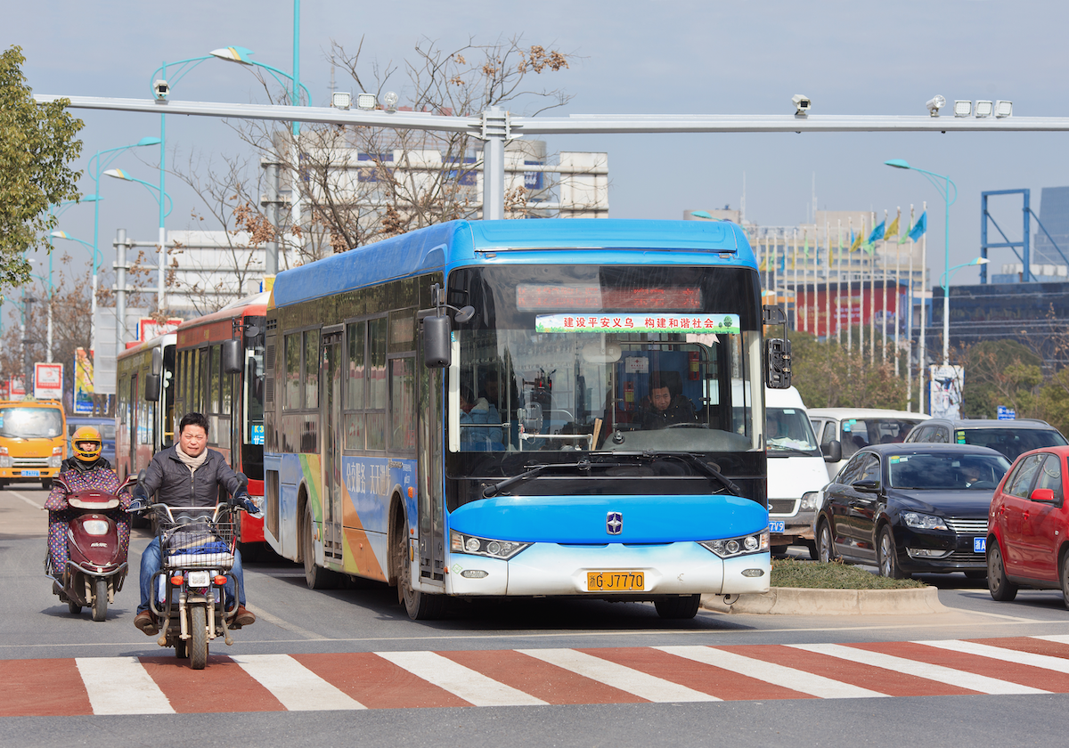 A bus in a city in China sits at a stop light with cars and motorbikes