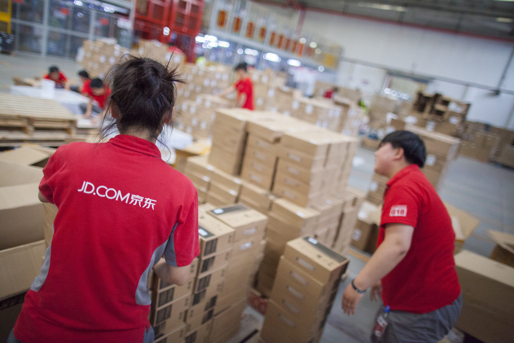 Two warehouse workers of JD.com sort packages, wearing red uniform shirts