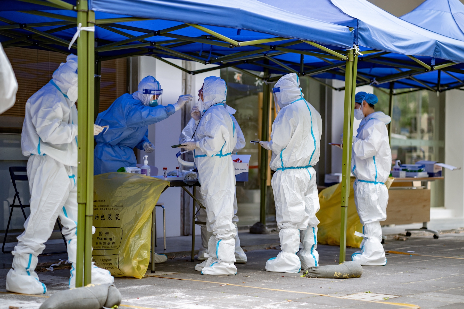 Workers dressed in white PPE take PCR tests under a tent