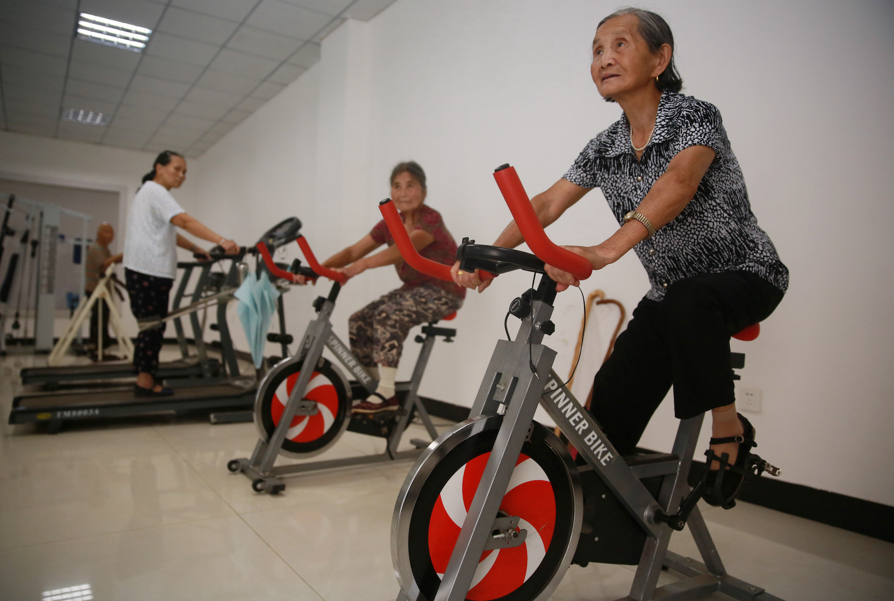 Older women ride stationary bicycles in a gym in China
