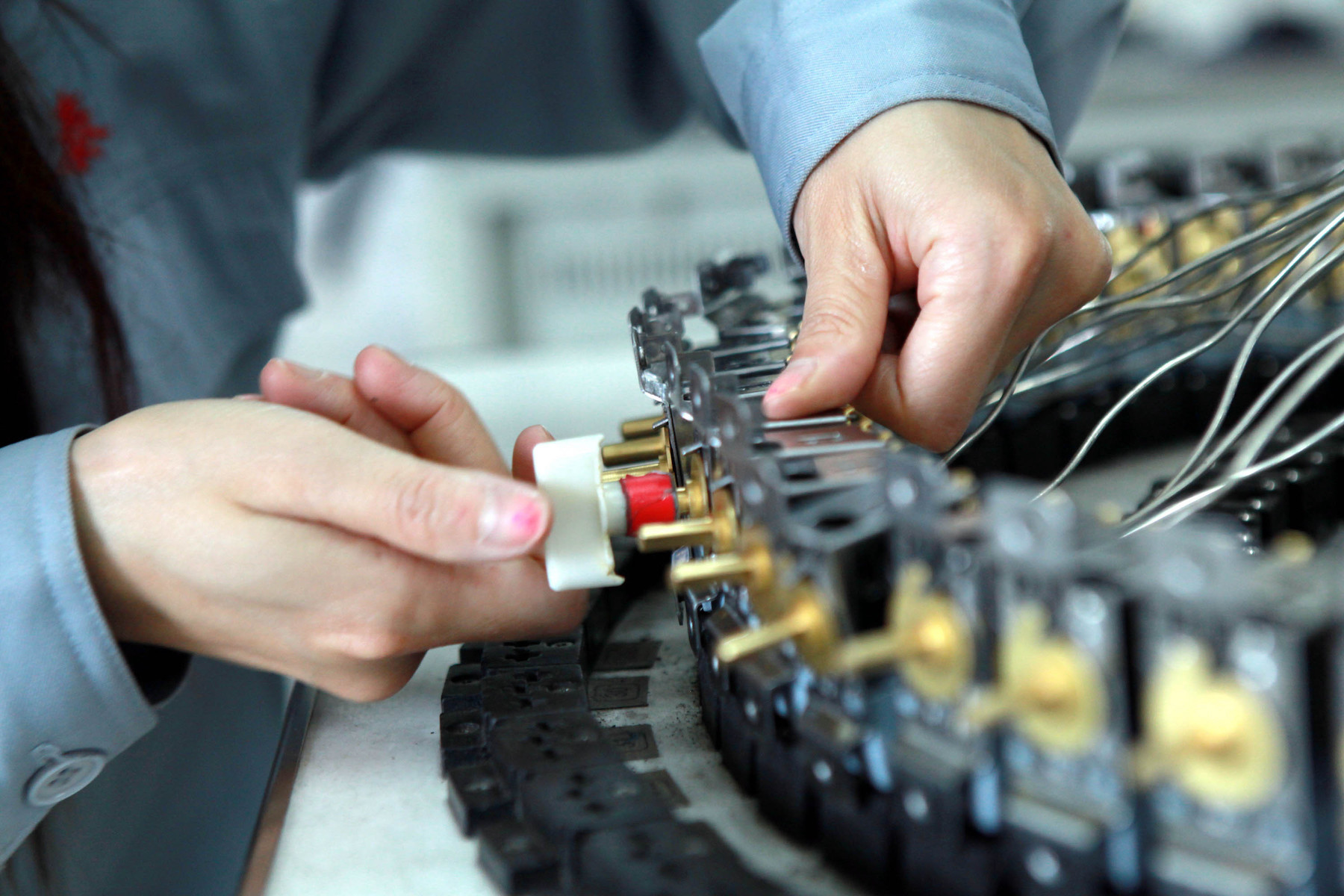 A close up photo of a worker's hands assembling a piece of electronics