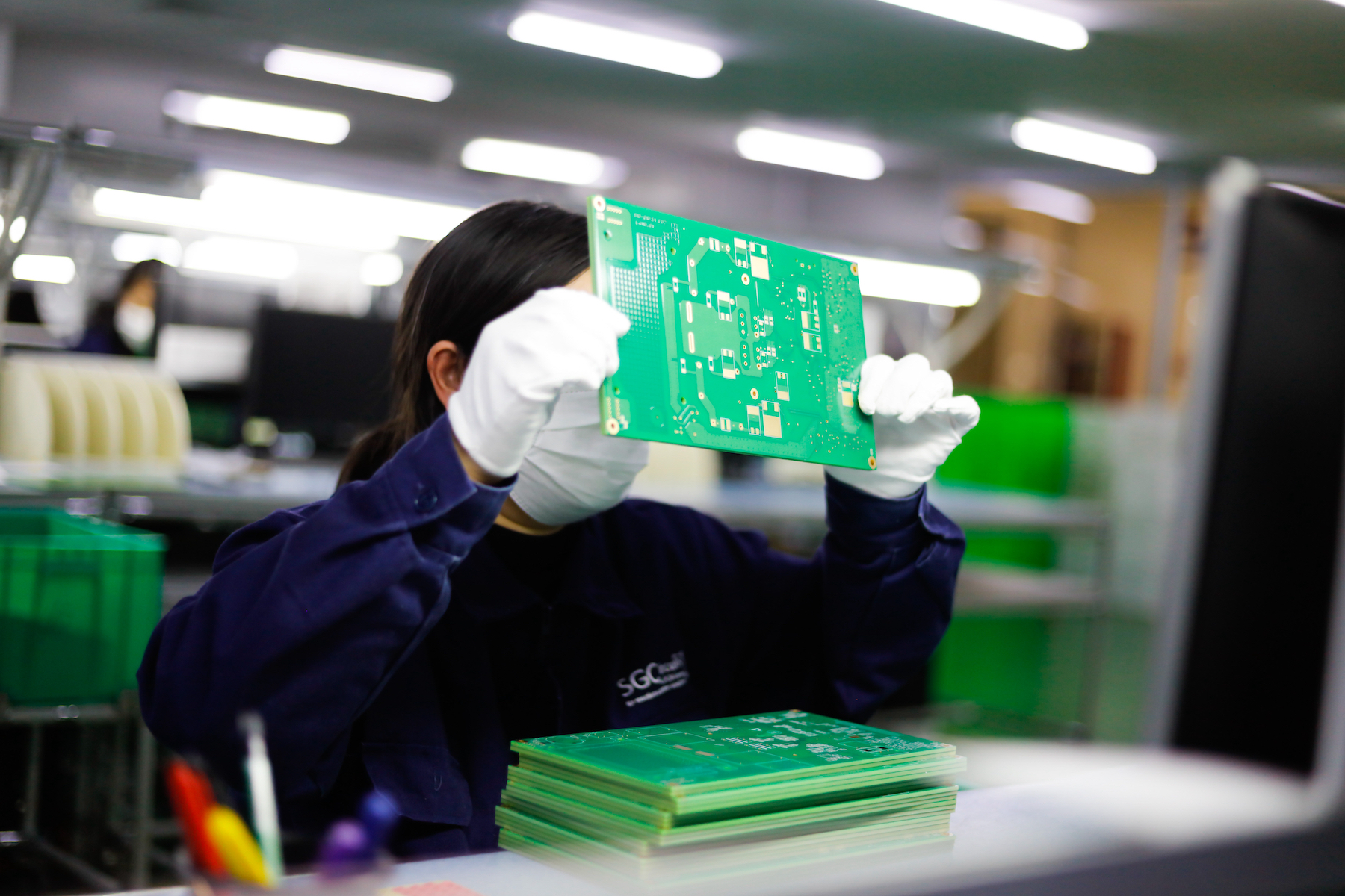 A worker holds up a circuit board in an electronics factory