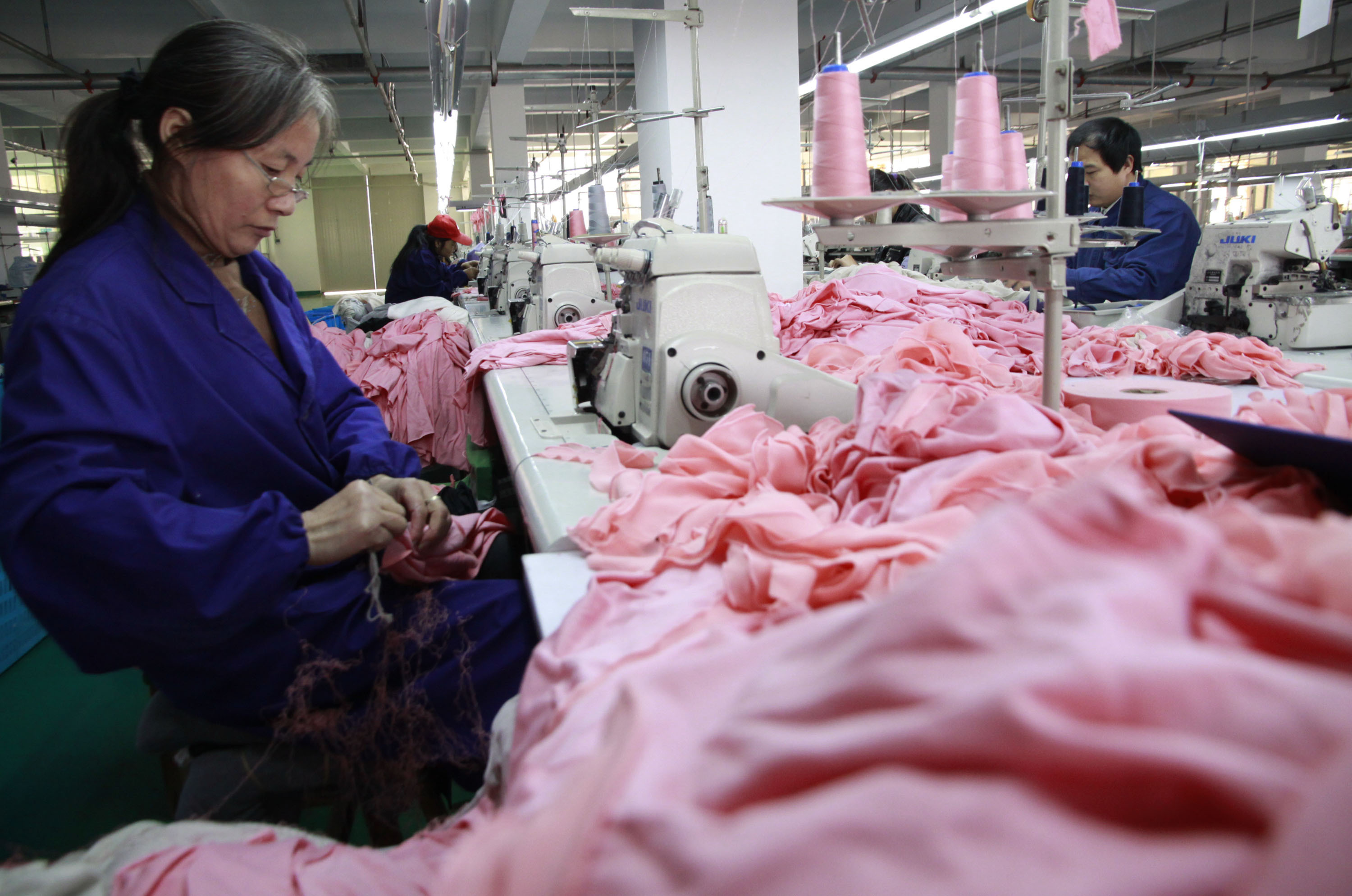 An older garment worker sews pink cloth in a factory