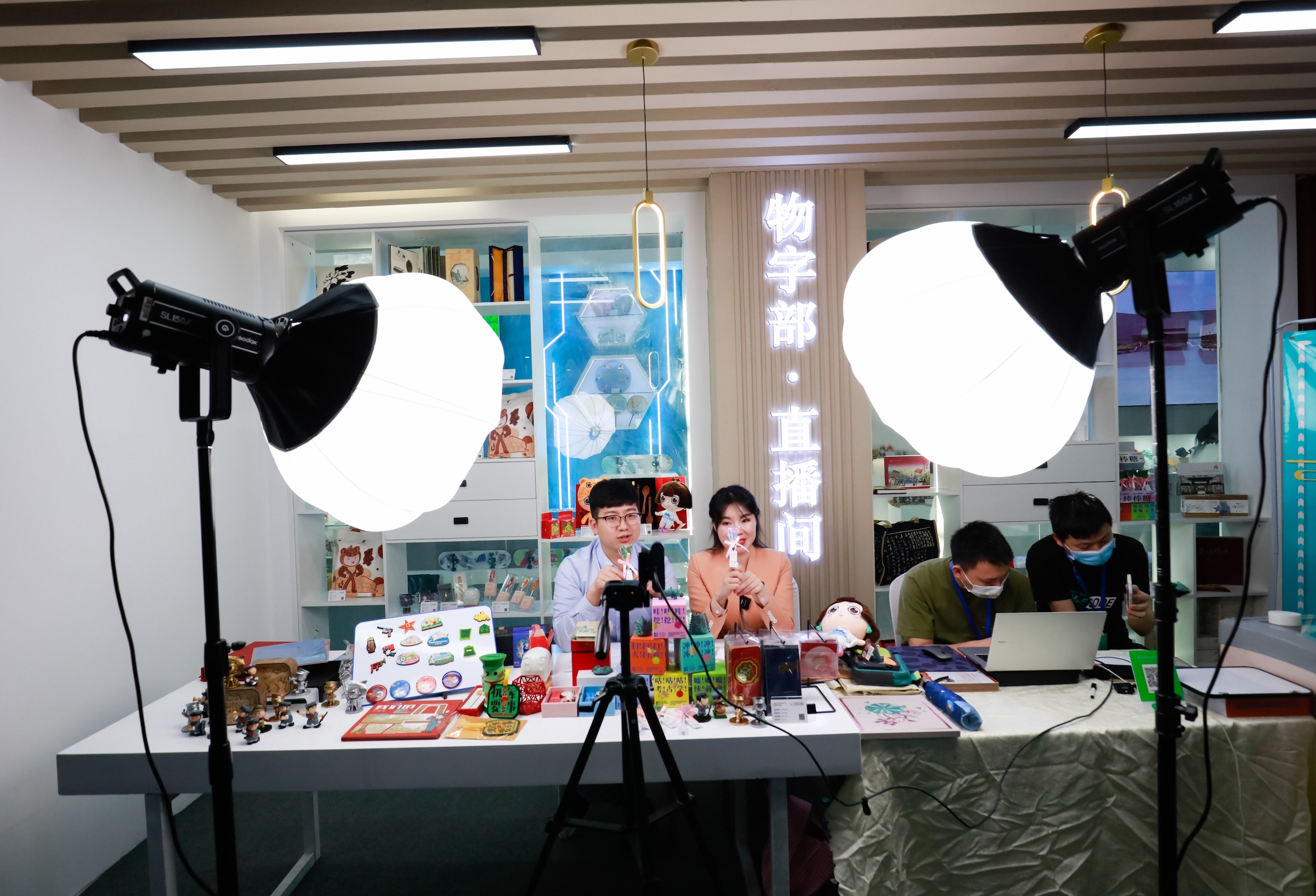 Behind the scenes of a livestream sales event, two hosts sit under bright lights and two technicians are to their side