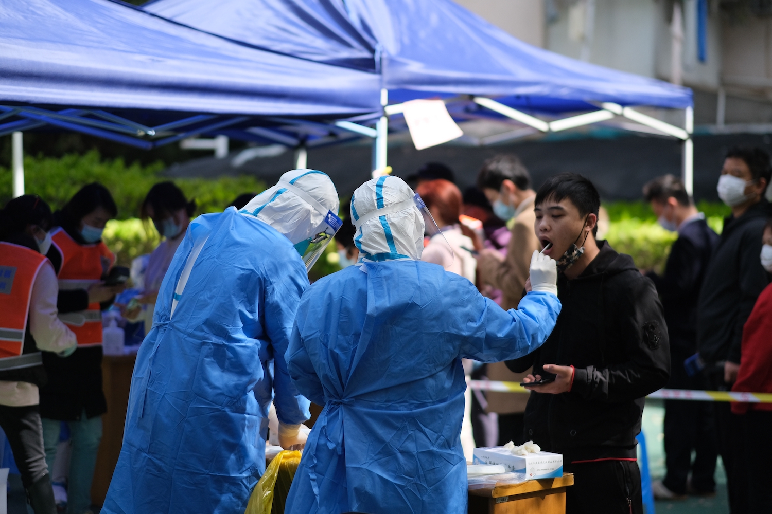 A resident has a PCR nucleic acid test taken by two medical workers dressed in blue PPE gowns