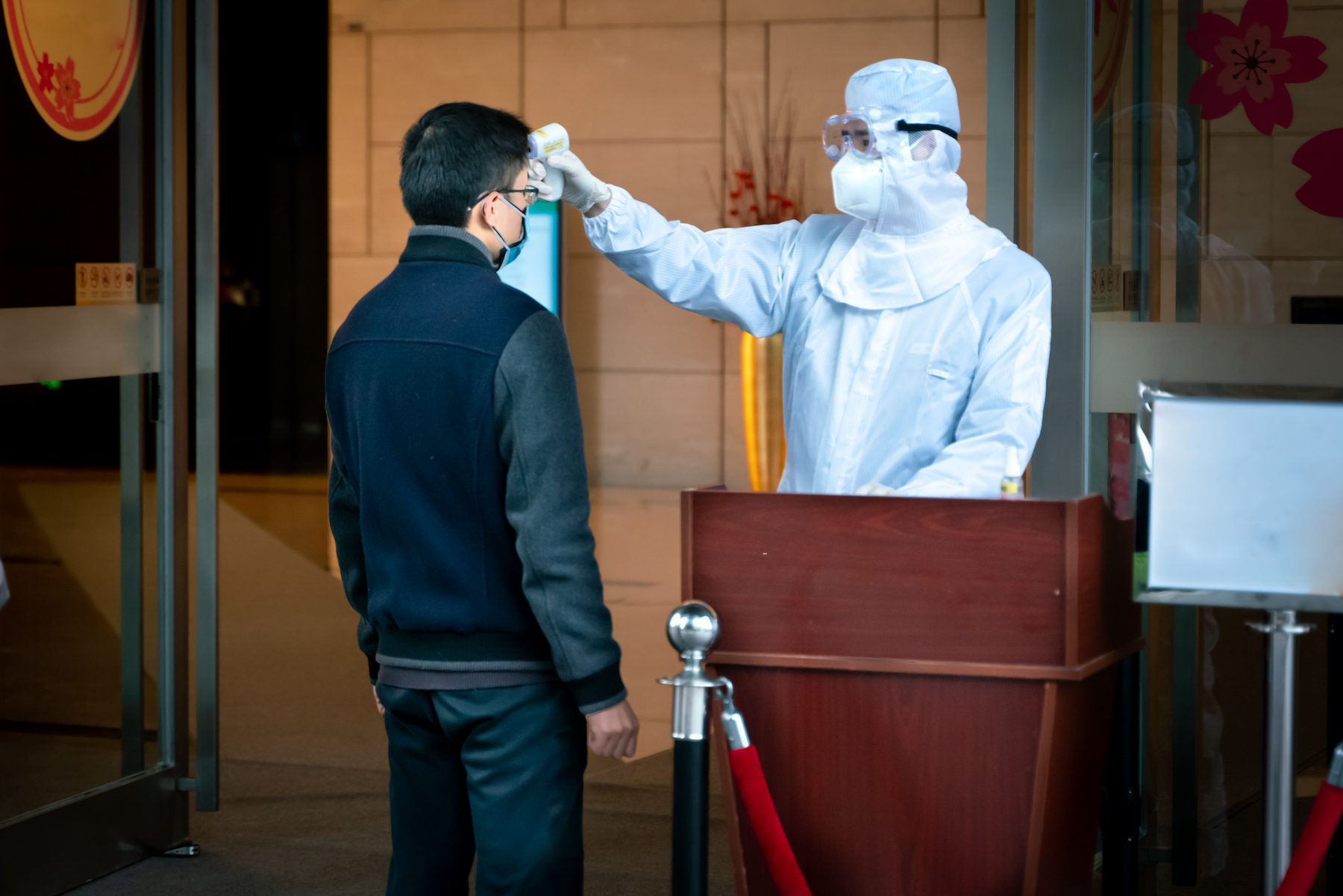 A security worker in PPE checks the temperature of those entering the building