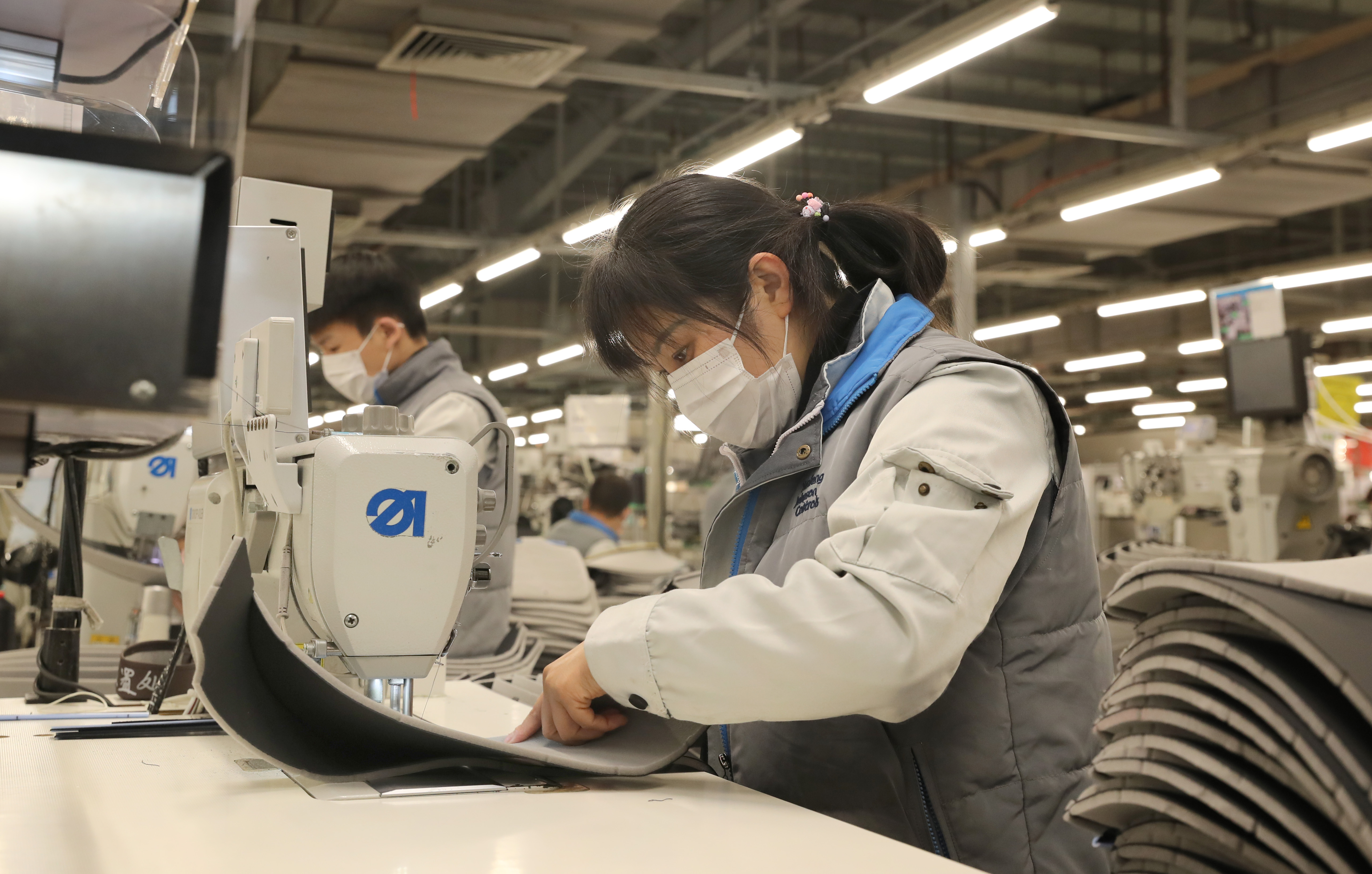 A young woman and man work side by side at sewing machines in a factory