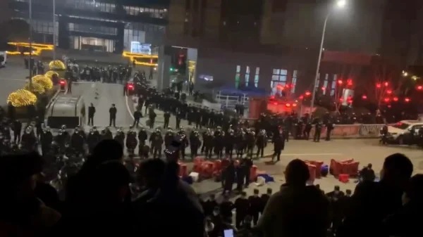 A grainy photo from social media shows a line of police officers in the road in front of road blocks a crowd of people